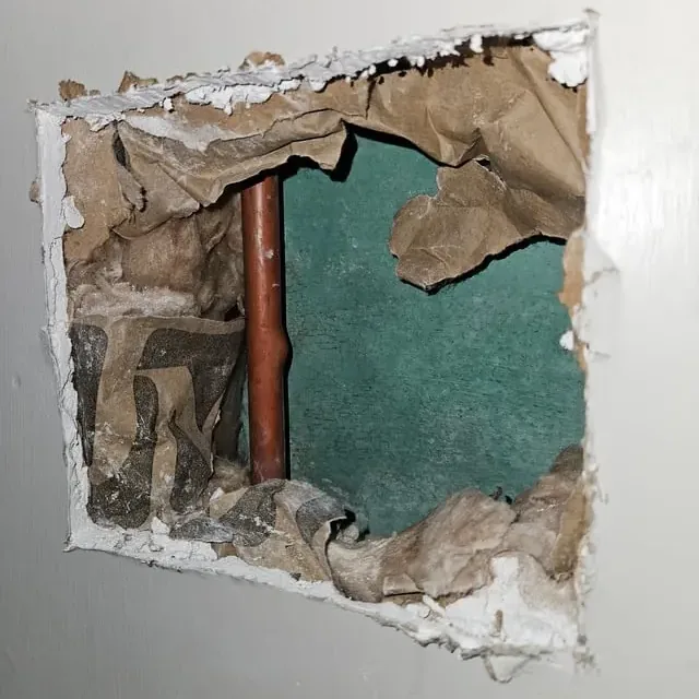 Opened drywall exposes a leaking copper supply pipe inside a wall