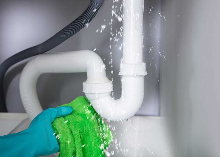 A gloved hand holding a rag trying to capture the water leaking from a pipe in King of Prussia